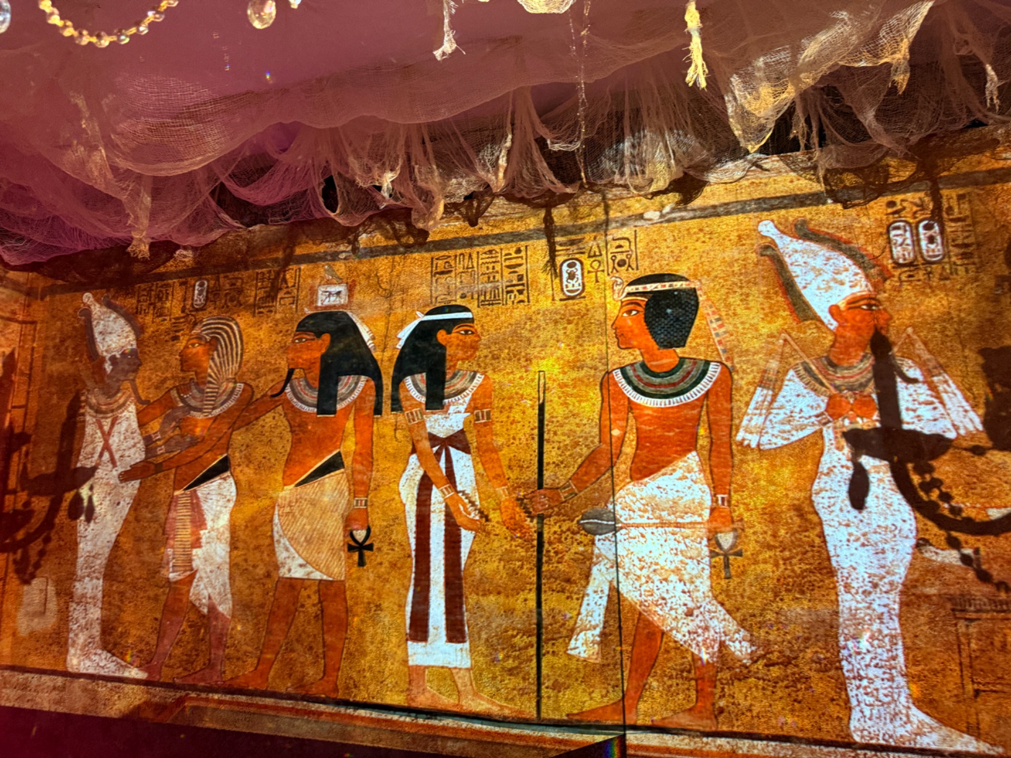 Golden Egyptian figures projected across the decorated wall beneath hanging gauze.
